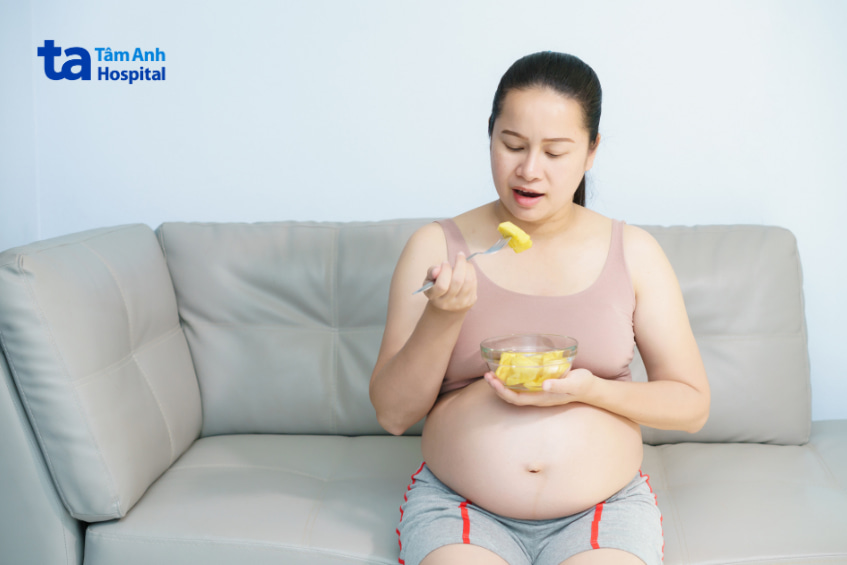 Bà bầu ngồi trên ghế ăn dứa tươi bằng nĩa, minh họa việc bầu ăn dứa có an toàn không