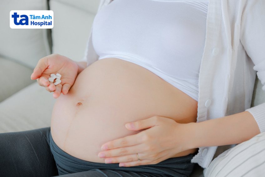 Phụ nữ mang thai đang ngồi xoa bụng và cầm viên bổ sung dưỡng chất