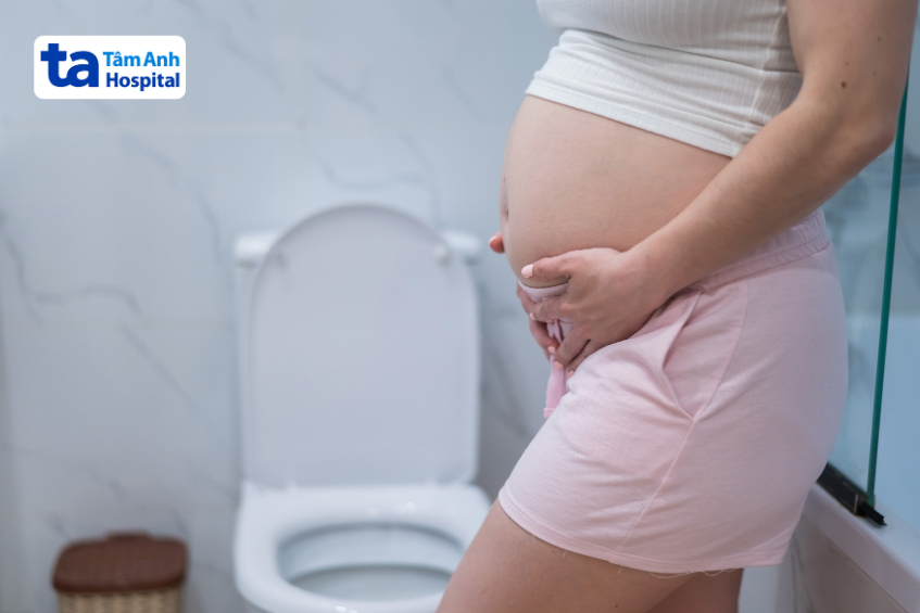 Bà bầu ôm bụng khó chịu đứng trước bồn cầu trong phòng vệ sinh