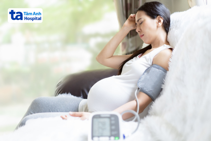 Phụ nữ mang thai ngồi mệt mỏi đo huyết áp tại nhà với máy đo điện tử
