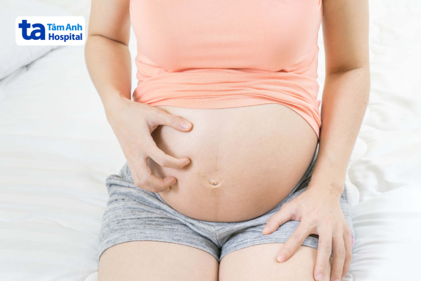 Bà bầu ngồi trên giường, tay chạm bụng, biểu hiện khó chịu nhẹ
