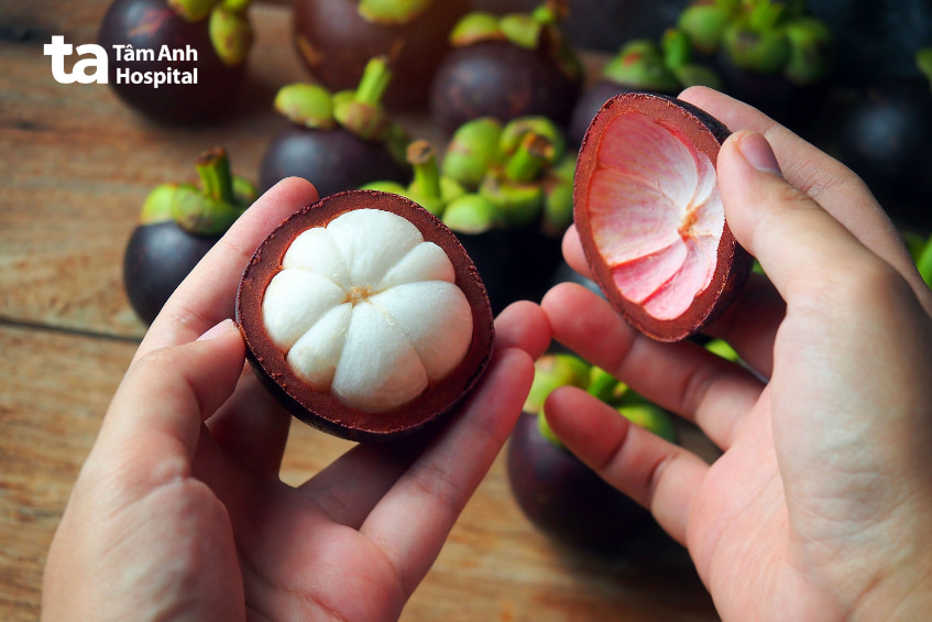 Cận cảnh hai tay cầm quả măng cụt bổ đôi, lộ rõ phần thịt trắng mọng nước