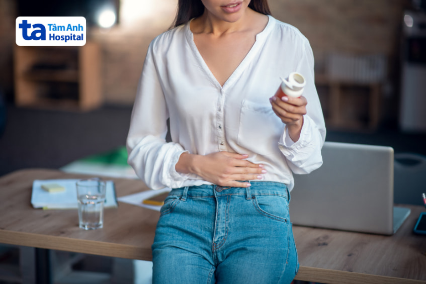Người phụ nữ bị đầy hơi, đau bụng và đang cầm lọ thuốc hỗ trợ tiêu hóa trên tay.