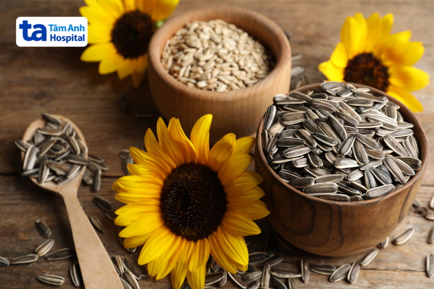 Hạt hướng dương và hạt bí trong bát gỗ cùng hoa hướng dương, bổ sung vitamin E cho mẹ bầu
