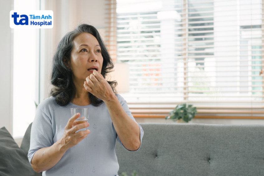 Người phụ nữ lớn tuổi đang uống thuốc điều trị bệnh tim tại nhà