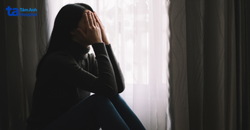 Người phụ nữ ôm mặt ngồi bên cửa sổ, biểu hiện căng thẳng có thể liên quan đến rối loạn thần kinh.