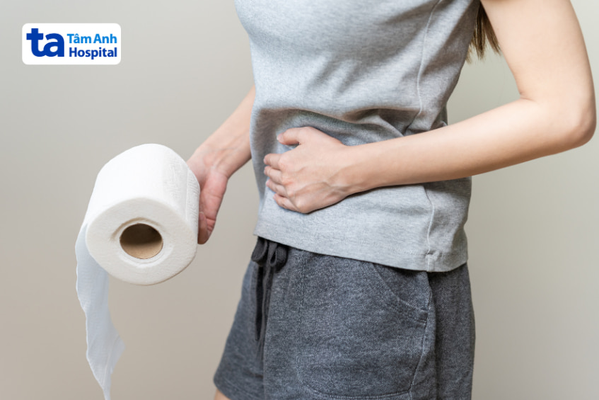 Người phụ nữ ôm bụng, cầm cuộn giấy vệ sinh do gặp vấn đề tiêu hóa hoặc táo bón.