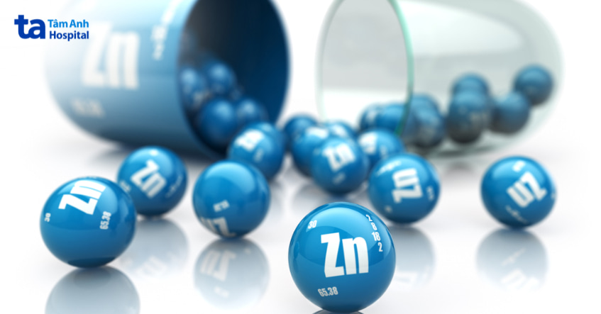 Viên kẽm màu xanh với ký hiệu Zn đổ ra từ lọ thủy tinh, biểu tượng cho thực phẩm bổ sung kẽm.