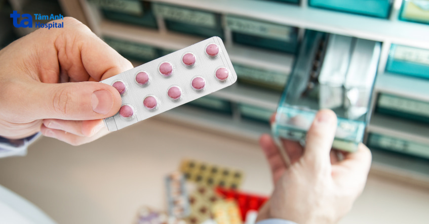 Nhân viên y tế cầm vỉ thuốc viên màu hồng tại quầy dược