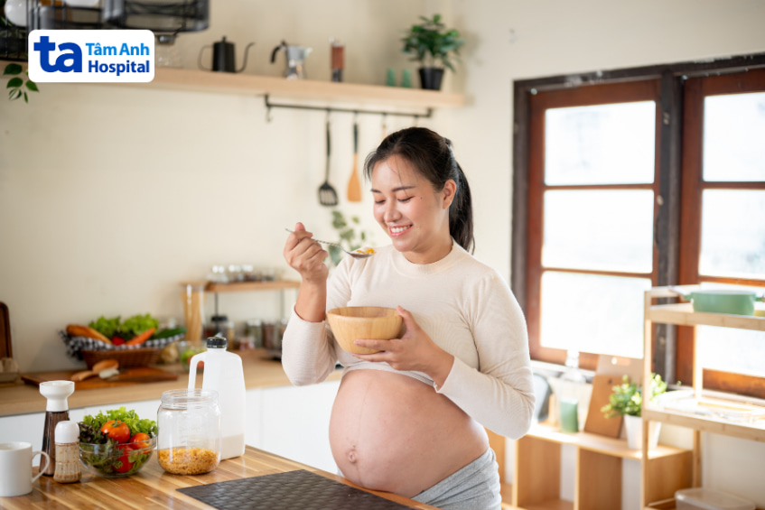 Phụ nữ mang thai cười tươi khi ăn sáng trong không gian bếp ấm cúng, truyền tải sự khỏe mạnh