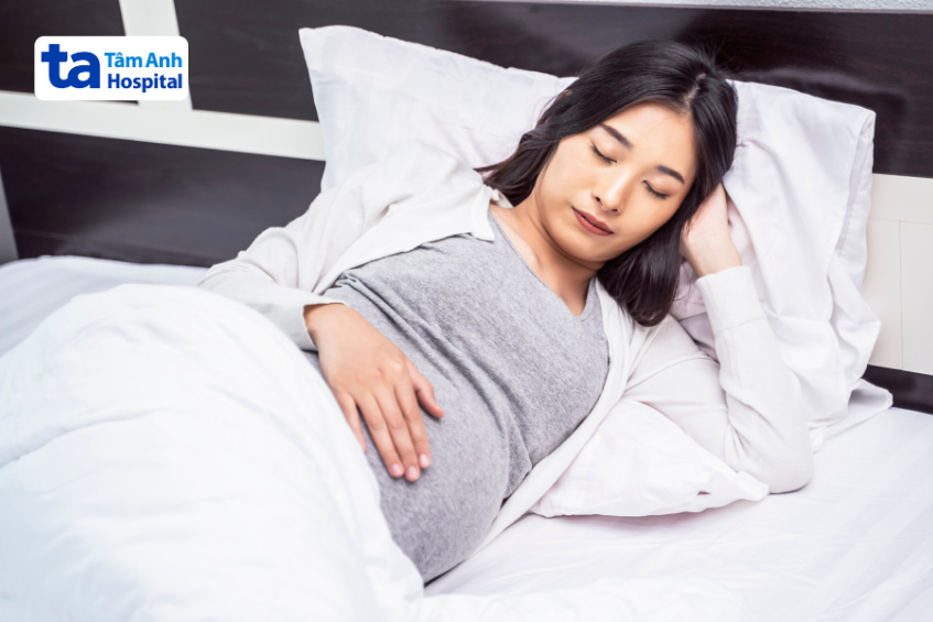 Phụ nữ mang thai nằm nghỉ ngơi trên giường, tay đặt nhẹ lên bụng
