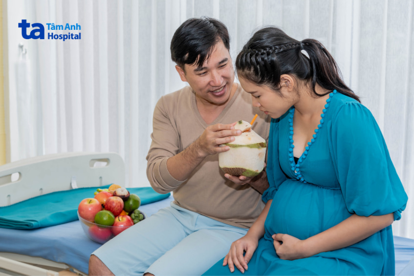 Người chồng đang đỡ trái dừa cho vợ bầu uống nước trong bệnh viện Tâm Anh