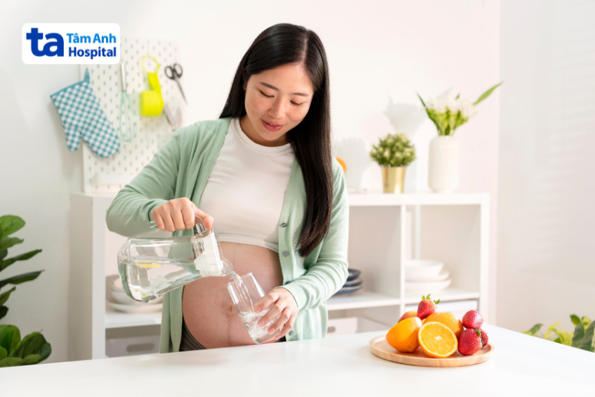 Phụ nữ mang thai rót nước lọc vào ly để đảm bảo đủ nước mỗi ngày trong thai kỳ