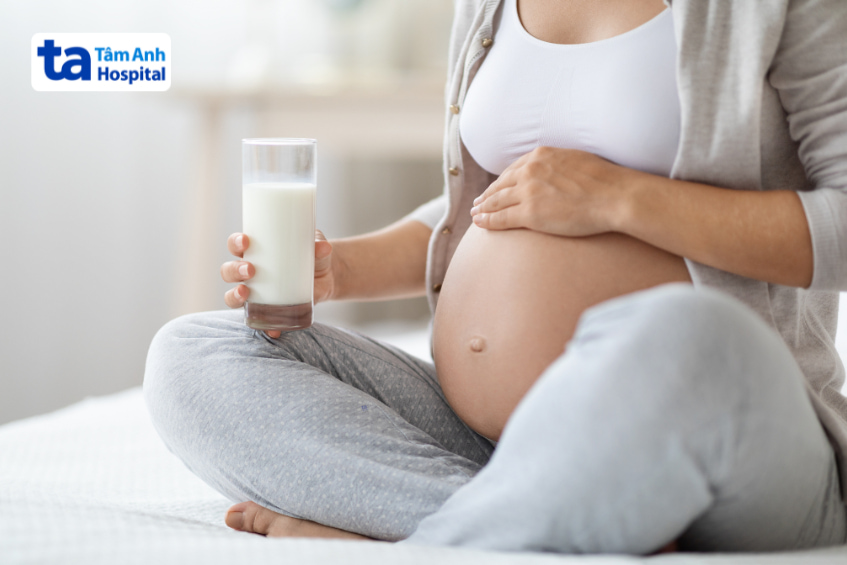 Mẹ bầu ngồi trên giường uống sữa, bổ sung canxi cần thiết cho sự phát triển thai nhi