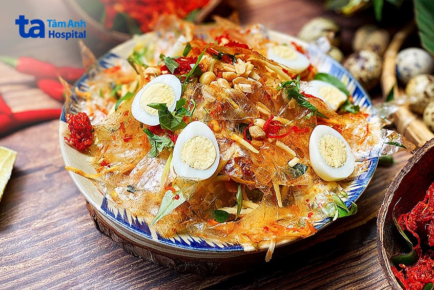 Bánh tráng trộn đầy đủ topping: trứng cút, xoài chua, lạc rang, rau thơm trên bàn gỗ