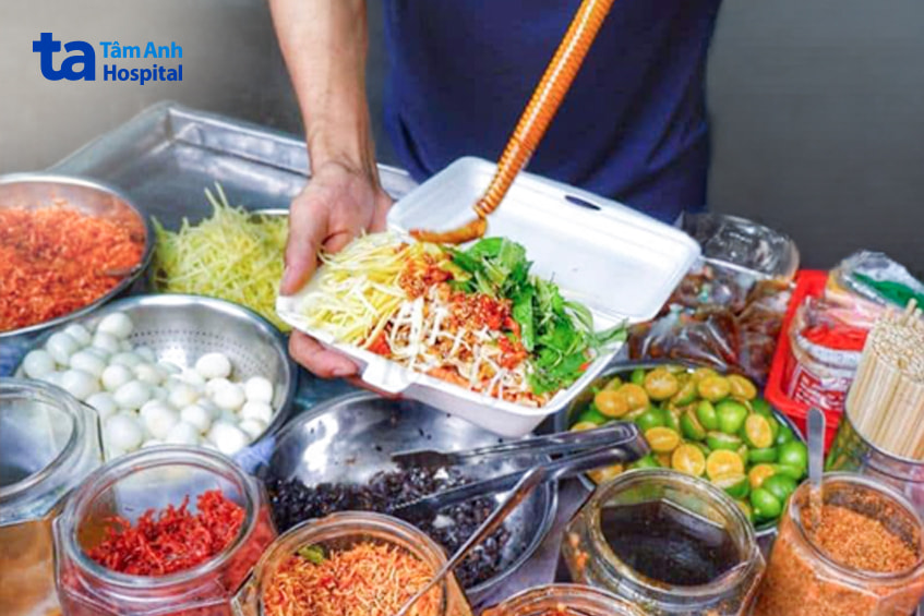 Người bán đang chế biến bánh tráng trộn với nhiều nguyên liệu như trứng cút, xoài, rau răm