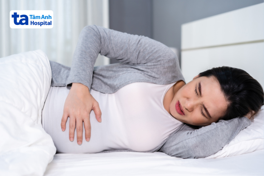 Bà bầu nằm trên giường với vẻ mặt đau bụng, biểu hiện khó chịu ở vùng bụng dưới