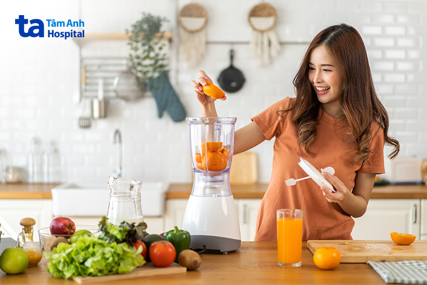 Người phụ nữ đang chuẩn bị nước ép cam trong bếp với nhiều rau củ xung quanh