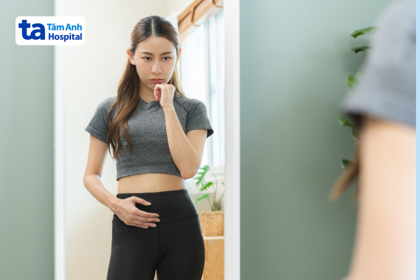 Cô gái chạm tay vùng bụng, lo lắng khi dùng thuốc điều trị mỡ máu
