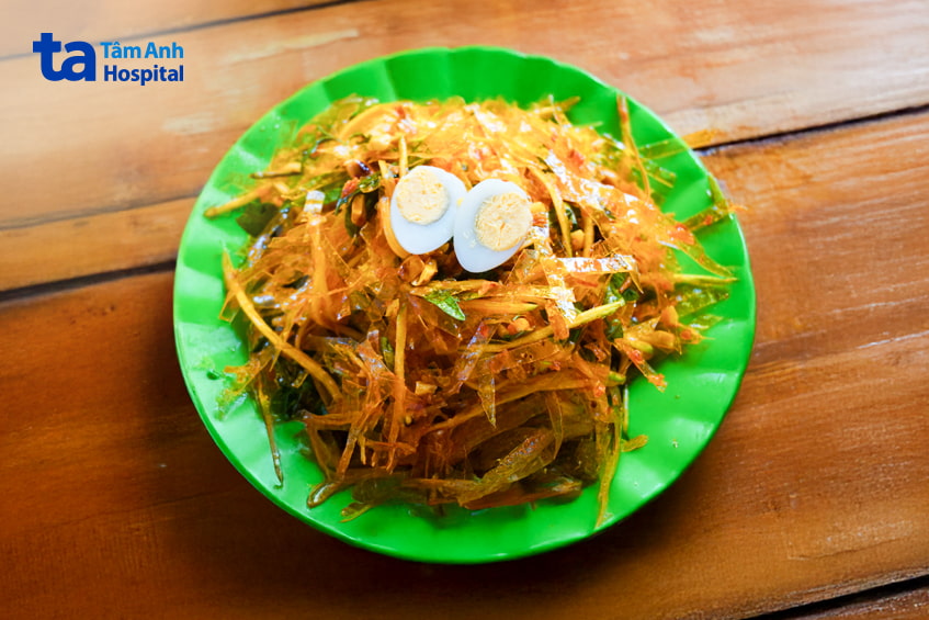 Dĩa bánh tráng trộn với trứng cút, rau răm, xoài bào trên bàn gỗ - món ăn vặt quen thuộc giới trẻ
