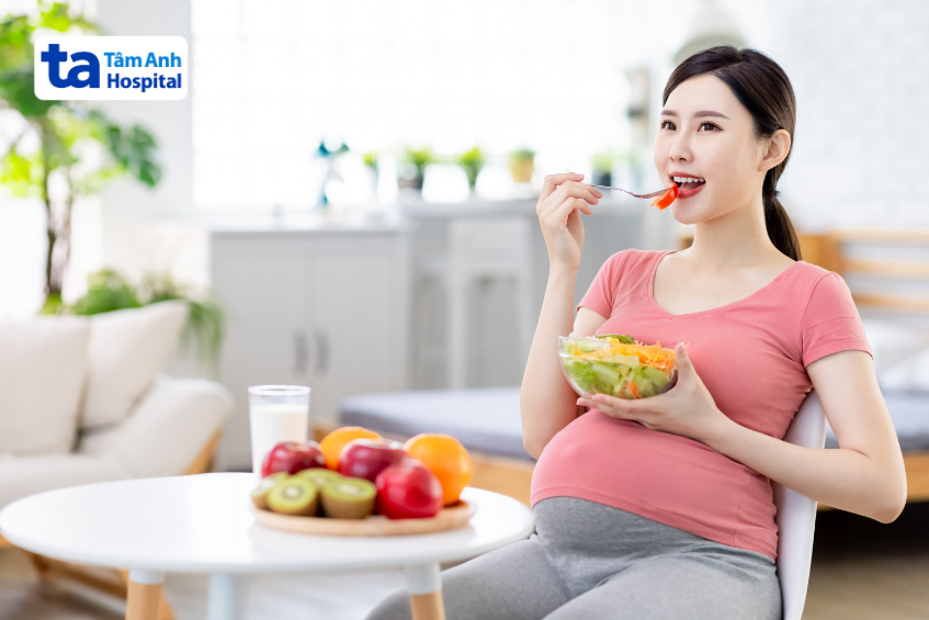 Mẹ bầu ăn salad trái cây tươi với kiwi, táo, cam trong không gian sáng sủa