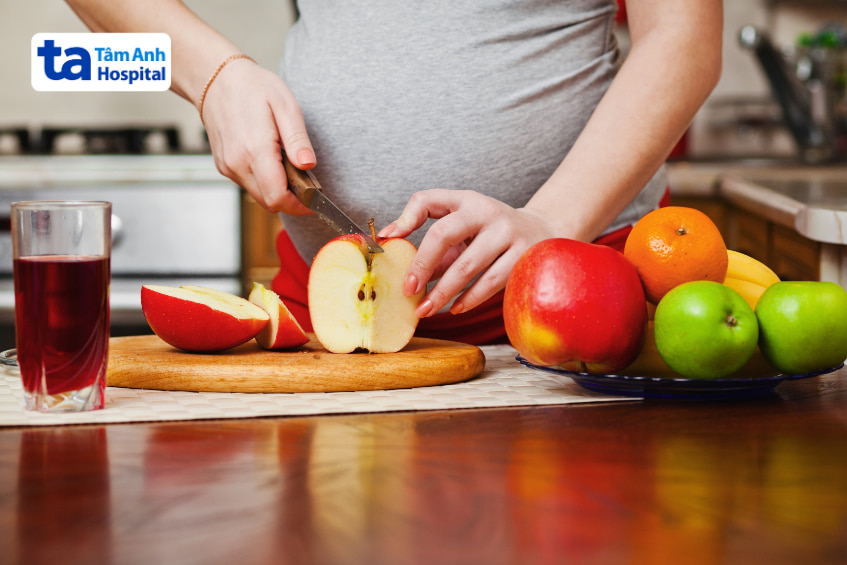 Mẹ bầu đang cắt táo và chuẩn bị đĩa trái cây tươi trong gian bếp