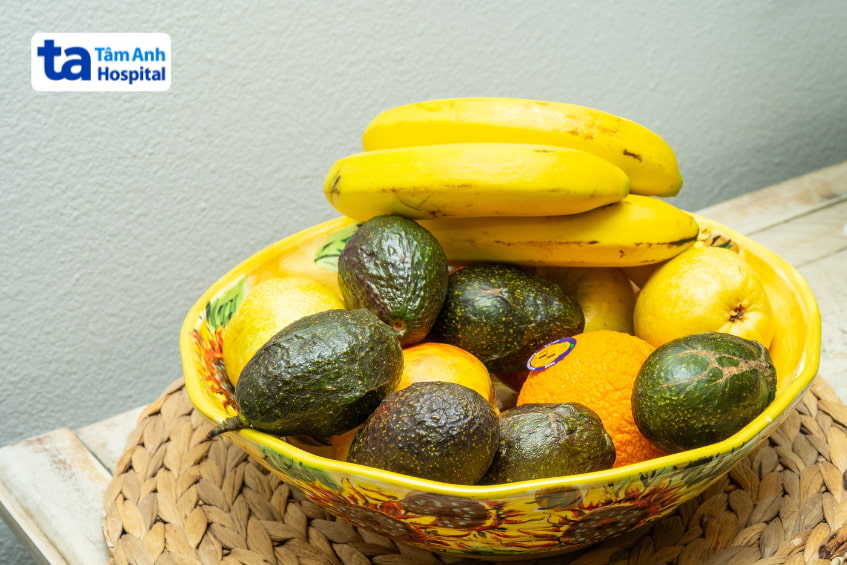 Đĩa trái cây gồm chuối, bơ, cam và chanh, giàu chất xơ tốt cho người sau mổ mật
