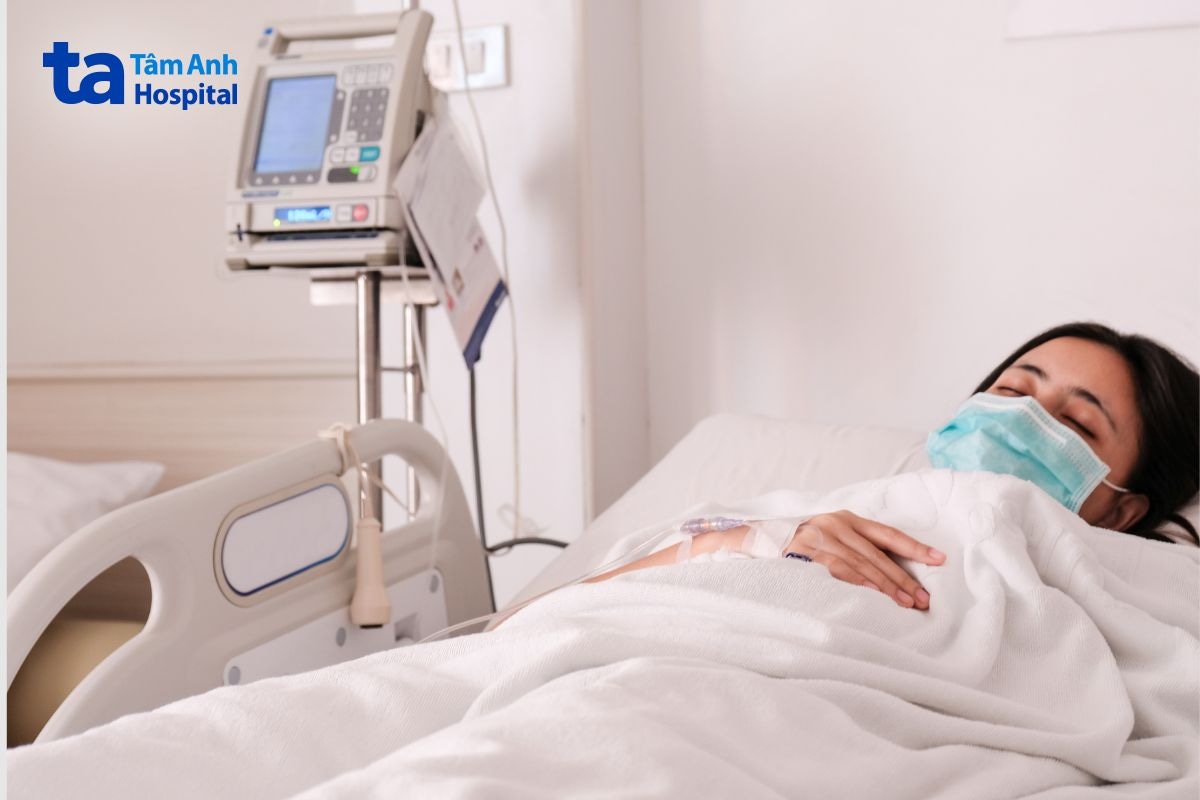 Người bệnh nằm trên giường với đường truyền tĩnh mạch và thiết bị theo dõi.