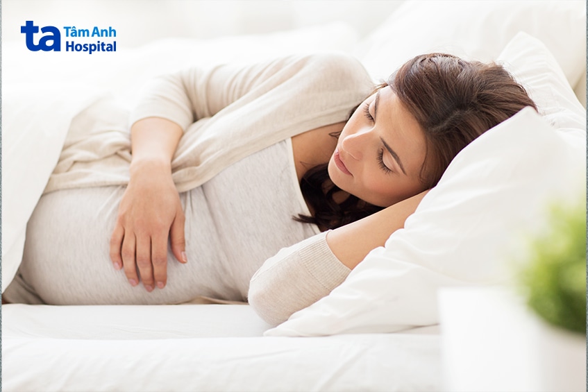 Mẹ bầu nằm nghỉ trên giường với tay đặt nhẹ lên bụng.
