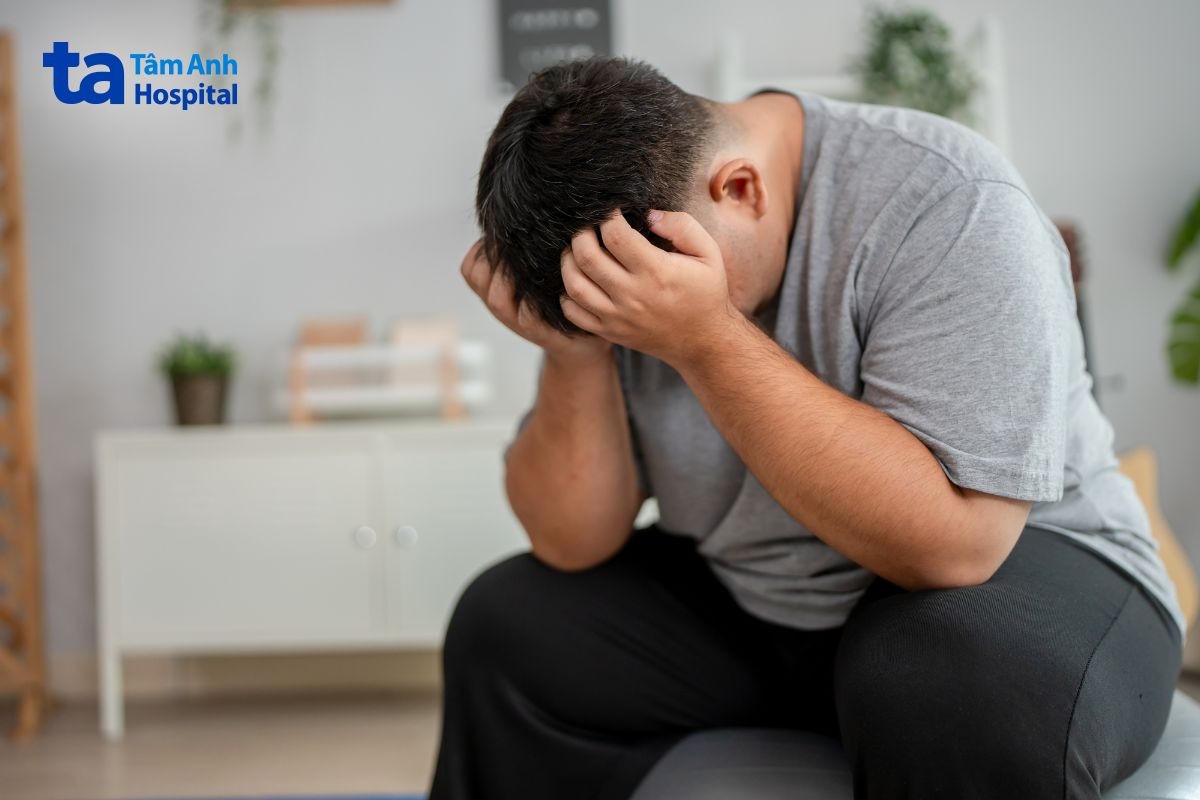 Người đàn ông thừa cân ngồi ôm đầu trong trạng thái mệt mỏi.