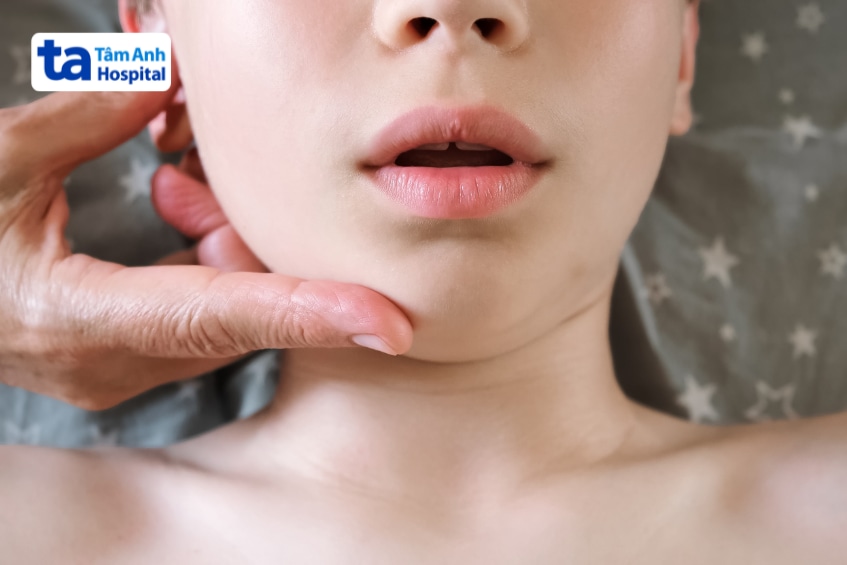 Bác sĩ dùng tay kiểm tra vùng cằm và khớp hàm của người bệnh đang há miệng