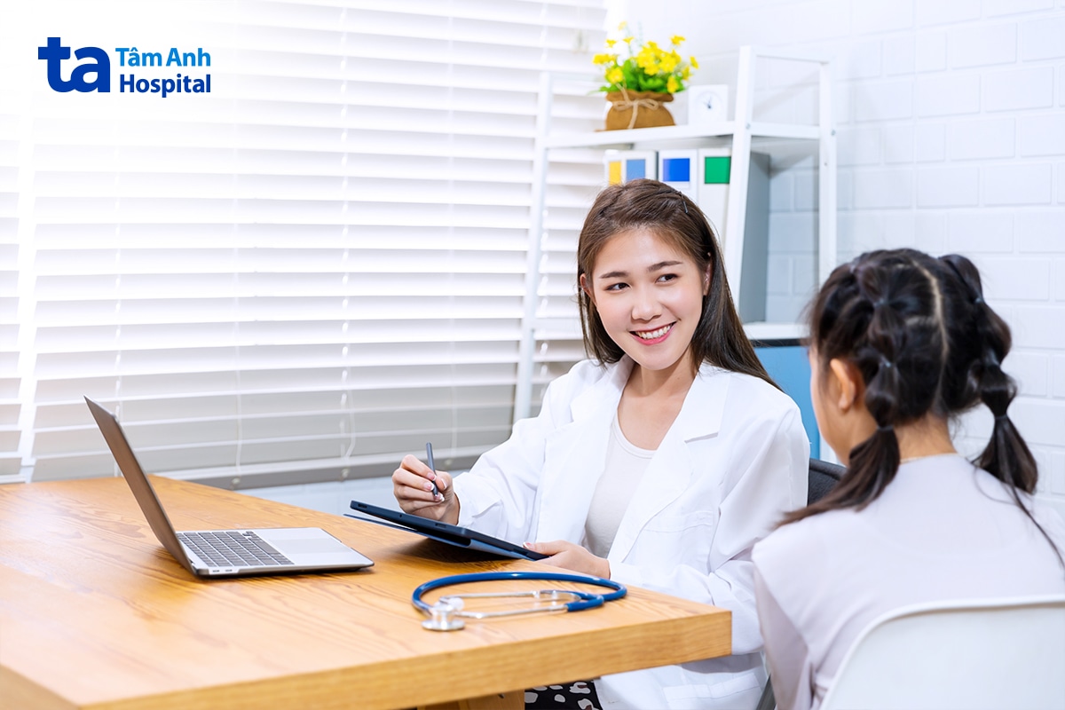 Bác sĩ cầm bút trao đổi với bé gái trong phòng khám