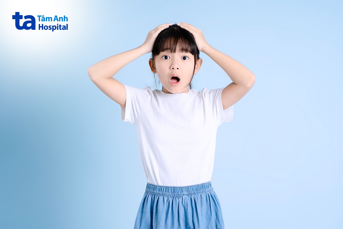 Bé gái ôm đầu với vẻ mặt ngạc nhiên, lo lắng trên nền xanh