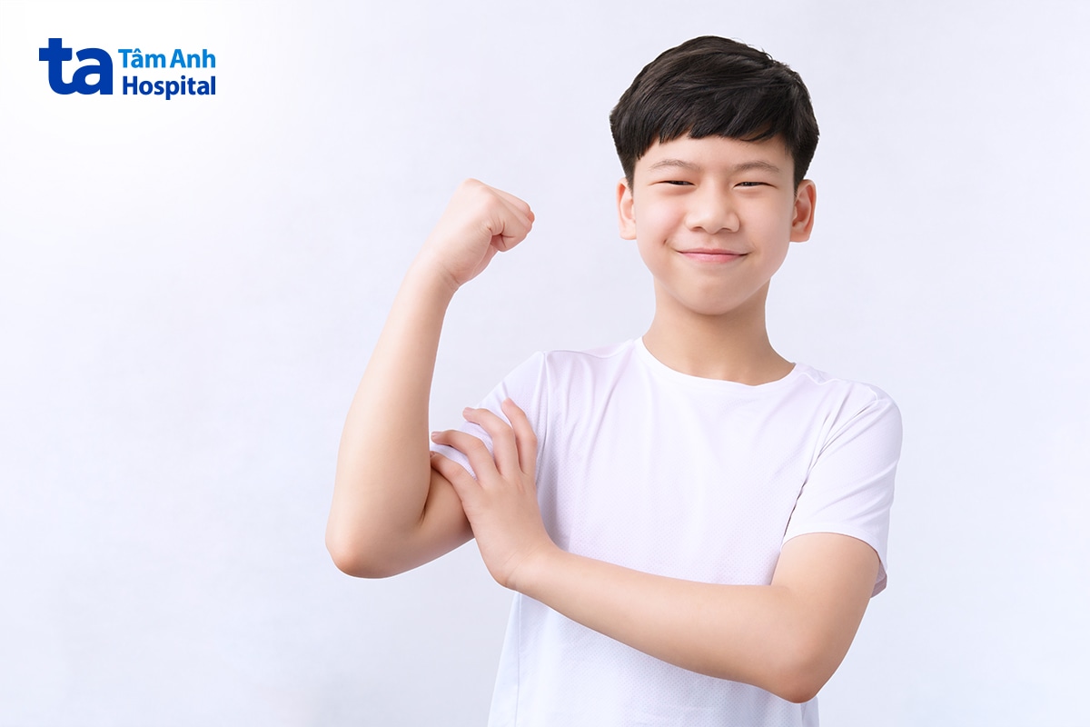 Bé Trai Gồng Cơ Tay Thể Hiện Sức Khỏe Trên Nền Sáng.