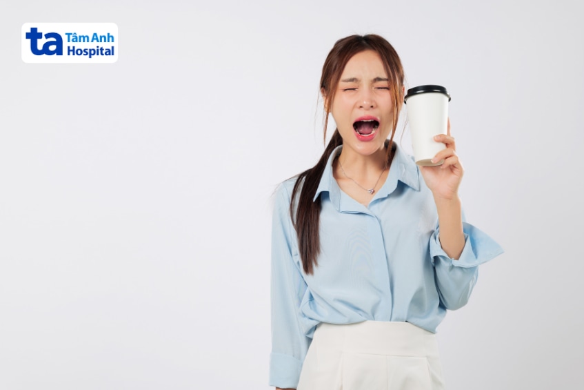 Cô gái há miệng to ngáp trong lúc cầm ly cà phê trên tay.