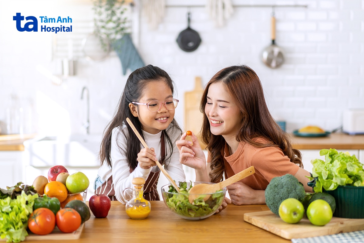 Mẹ và bé gái cùng trộn salad rau củ quả tươi trong gian bếp