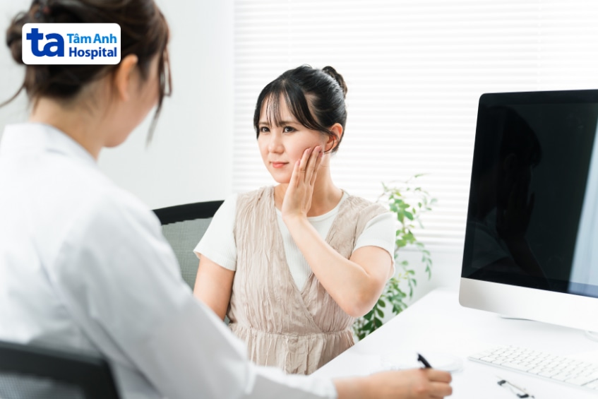 Người bệnh ôm má đau hàm khi ngồi khám với bác sĩ tại phòng khám