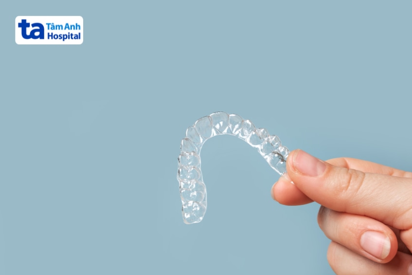Bàn tay cầm máng nhai nhựa trong suốt trên nền xanh